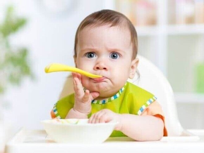 criança sentada em uma cadeira de alimentação com expressão curiosa enquanto come.