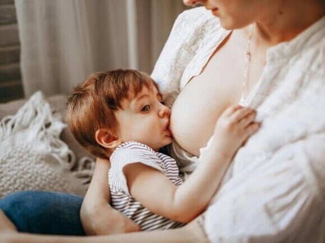 Close-up de uma mãe em uma camisa branca amamentando seu filho (cerca de 1 a 2 anos) dentro de casa.