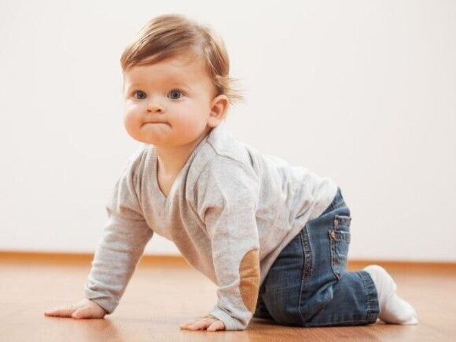 Um bebê engatinhando em um chão de madeira. Ele usa uma blusa cinza com cotoveleiras de camurça marrom e calça jeans. Um bebê engatinhando em um chão de madeira. Ele usa uma blusa cinza com cotoveleiras de camurça marrom e calça jeans.