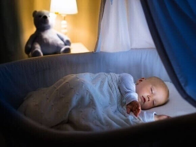 Bebê dormindo calmamente no berço à noite, sob uma luz amarela suave, representando um bebê que dorme bem.