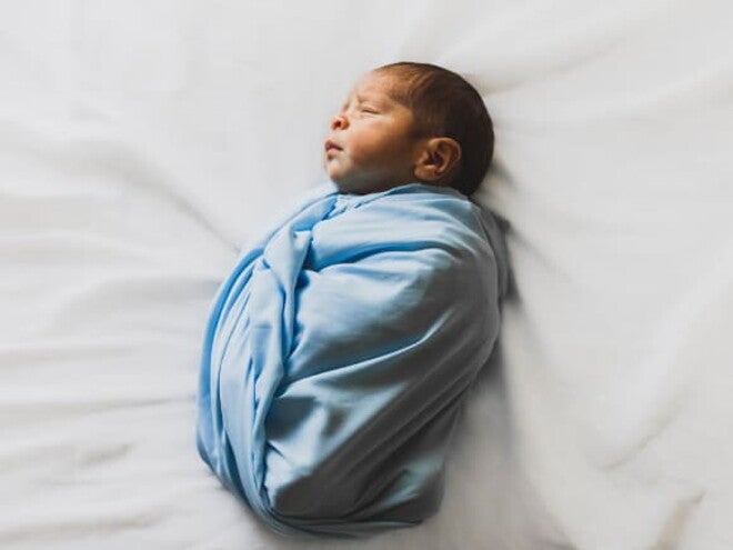 bebê sorrindo, com as mãos levantadas e parcialmente coberto por uma manta azul bebê sorrindo, com as mãos levantadas e parcialmente coberto por uma manta azul