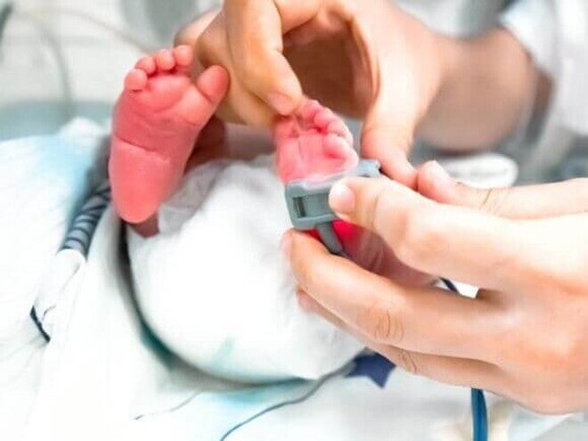 Pés de um bebê recém-nascido passando por uma avaliação pelas mão de um profissional da saúde.