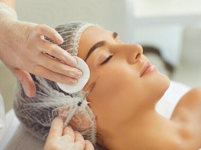 Close-up de uma mulher recebendo uma injeção de Botox ou preenchimento facial em uma clínica de estética, com a profissional usando luvas e uma seringa, representando o procedimento estético.