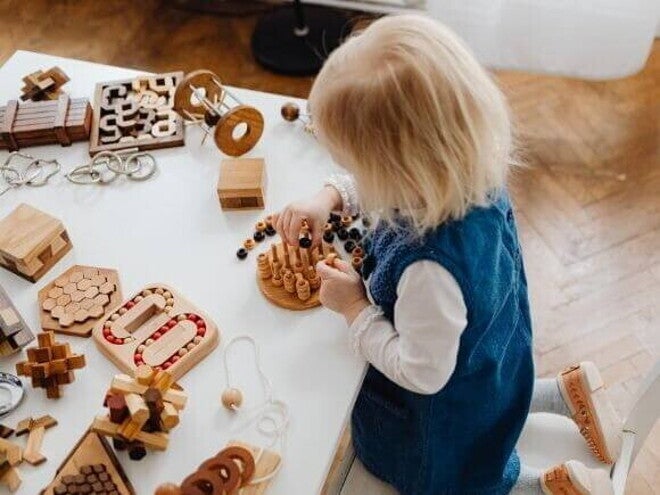 Uma criança está sentada em uma mesa branca e se diverte com uma série de brinquedos sensoriais de madeira. A cena foca no envolvimento da criança com as diferentes texturas e formas, ressaltando o tema de brincadeiras sensoriais. Uma criança está sentada em uma mesa branca e se diverte com uma série de brinquedos sensoriais de madeira. A cena foca no envolvimento da criança com as diferentes texturas e formas, ressaltando o tema de brincadeiras sensoriais.