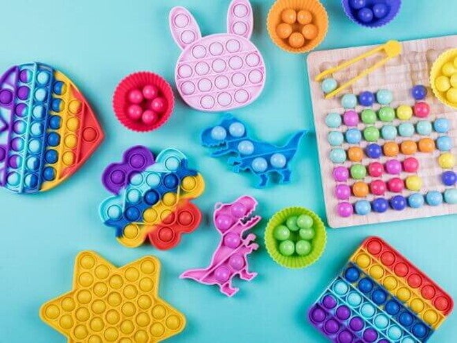 Diversos brinquedos sensoriais coloridos e de formas variadas, dispostos em uma superfície azul. Diversos brinquedos sensoriais coloridos e de formas variadas, dispostos em uma superfície azul.