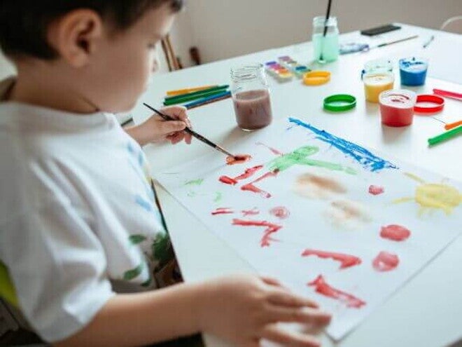 Criança canhota pintando uma folha branca com tinta e pincel Criança canhota pintando uma folha branca com tinta e pincel