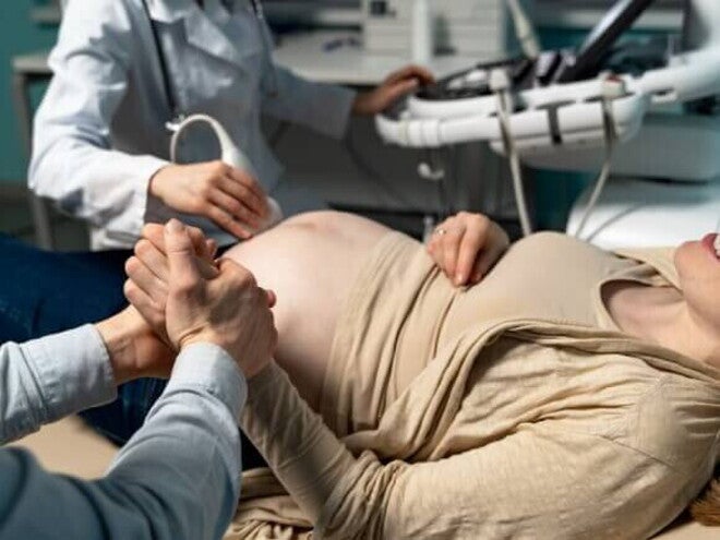Uma gestante deitada em um consultório médico, segurando a mão de um homem, durante um exame de ultrassom Uma gestante deitada em um consultório médico, segurando a mão de um homem, durante um exame de ultrassom