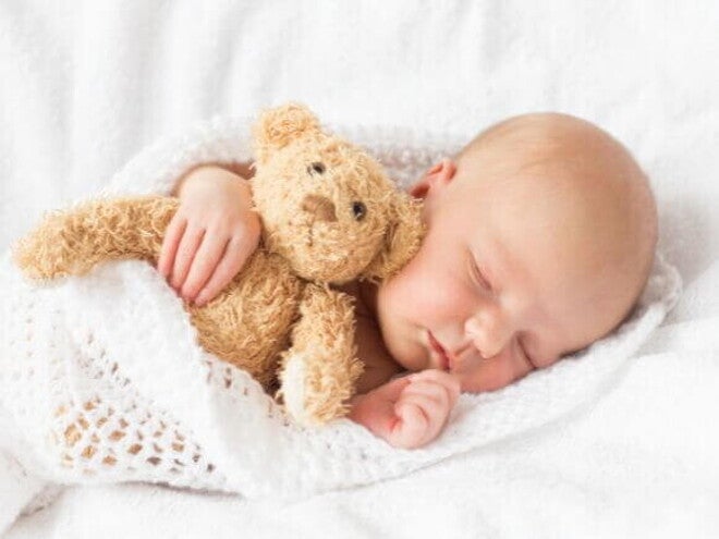 Bebê dormindo tranquilamente abraçado a um ursinho de pelúcia, enrolado em uma coberta branca de crochê Bebê dormindo tranquilamente abraçado a um ursinho de pelúcia, enrolado em uma coberta branca de crochê