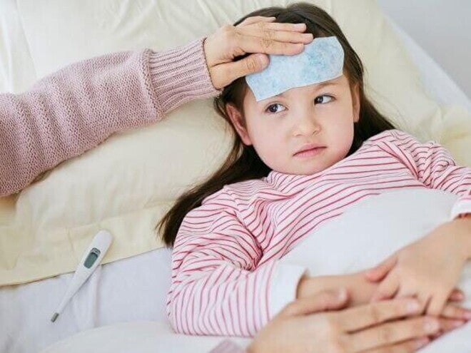 Criança doente deitada na cama com compressa na testa e termômetro ao lado Criança doente deitada na cama com compressa na testa e termômetro ao lado