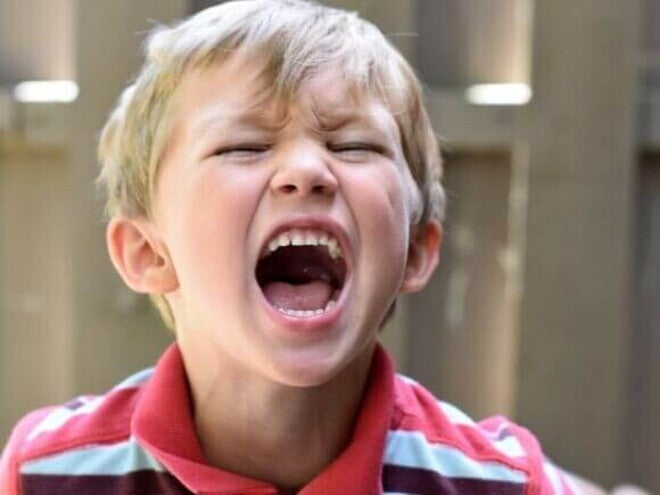 Close-up de uma criança gritando com a boca bem aberta e olhos fechados, expressando uma intensa explosão emocional ou crise de raiva.