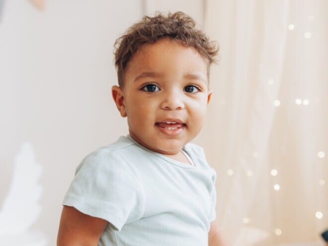 Criança vestindo blusa azul claro em um quarto de cores neutras e luzes de decoração Criança vestindo blusa azul claro em um quarto de cores neutras e luzes de decoração