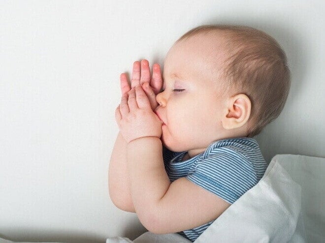 Um bebê dormindo, com as mãos perto do rosto, e o dedão da mão esquerda dentro da boca. Um bebê dormindo, com as mãos perto do rosto, e o dedão da mão esquerda dentro da boca.