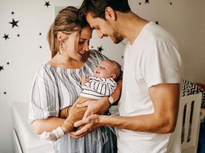 Um homem e uma mulher sorridentes seguram um bebê nos braços, dentro de um quarto infantil. Um homem e uma mulher sorridentes seguram um bebê nos braços, dentro de um quarto infantil.