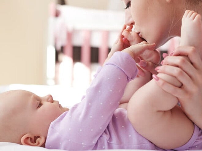 Mãe embalando carinhosamente as perninhas do seu bebê que está deitado na cama Mãe embalando carinhosamente as perninhas do seu bebê que está deitado na cama