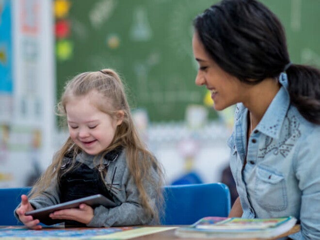 Criança com Síndrome de Down segurando um tablet ao lado da professora na escola Criança com Síndrome de Down segurando um tablet ao lado da professora na escola