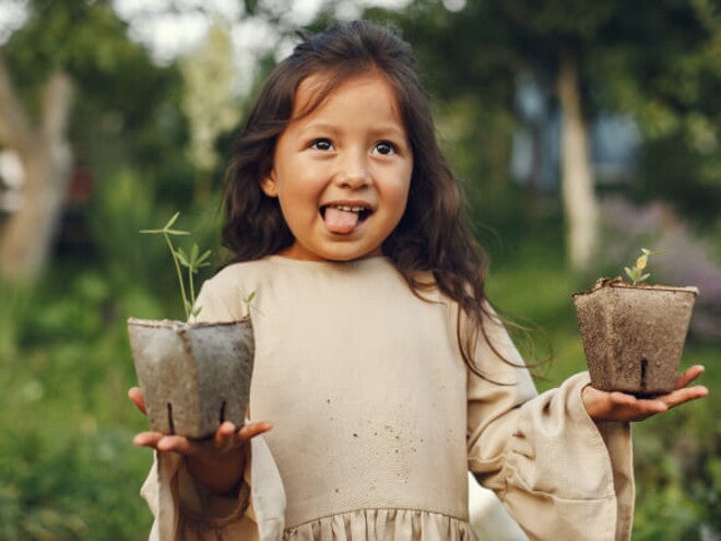 menina sorri e mostra a língua enquanto segura dois vasos de plantas menina sorri e mostra a língua enquanto segura dois vasos de plantas