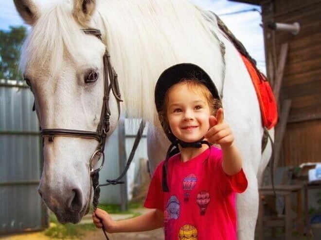 Menina sorrindo e apontando com o dedo, enquanto segura a rédea de um cavalo Menina sorrindo e apontando com o dedo, enquanto segura a rédea de um cavalo