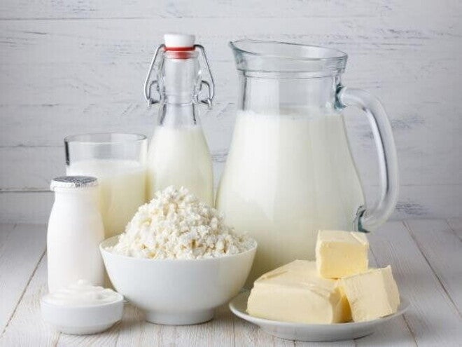 Imagem com leite, queijo, manteiga e outros derivados do leite dispostos sobre uma mesa clara, representando alimentos associados à proteína do leite.