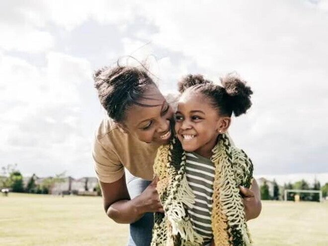 Mãe e filha rindo abraçadas em um campo de futebol