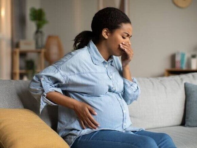 Mulher grávida sentada em um sofá, com uma mão na barriga e a outra mão na boca. Mulher grávida sentada em um sofá, com uma mão na barriga e a outra mão na boca.