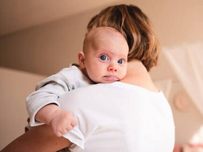 Bebê com refluxo regurgitando após a mamada no ombro da mãe. ‌