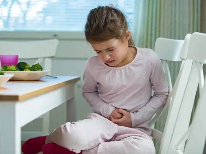 Menina com intoxicação alimentar, sentada à mesa de jantar, reagindo à dor, colocando as mãos na barriga Menina com intoxicação alimentar, sentada à mesa de jantar, reagindo à dor, colocando as mãos na barriga