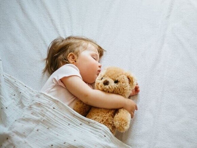 Uma bebê deitada em uma cama, dormindo, abraçada com um ursinho de pelúcia. Uma bebê deitada em uma cama, dormindo, abraçada com um ursinho de pelúcia.
