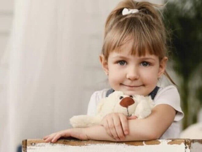 Menina de aproximadamente 4 anos apoiada na mesa abraçada com seu ursinho de pelúcia Menina de aproximadamente 4 anos apoiada na mesa abraçada com seu ursinho de pelúcia
