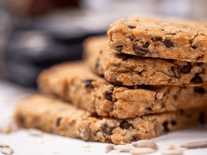 Barras de cereais empilhadas com gotas de chocolate e sementes visíveis.