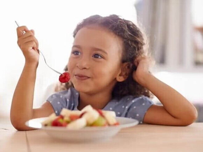 Lanchinho: o que a criança pode comer à noite para dormir bem Representando bons hábitos alimentares, uma criança come seu lanchinho: várias frutas picadas em um prato.