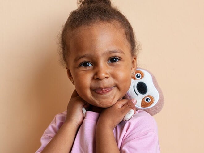 Menina sorrindo vestindo blusa lilás e segurando um bicho preguiça de pelúcia Menina sorrindo vestindo blusa lilás e segurando um bicho preguiça de pelúcia