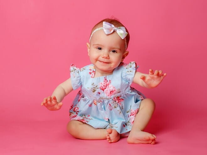 Bebê usando vestido florido e laço na cabeça em um ambiente com fundo cor de rosa. Bebê usando vestido florido e laço na cabeça em um ambiente com fundo cor de rosa.