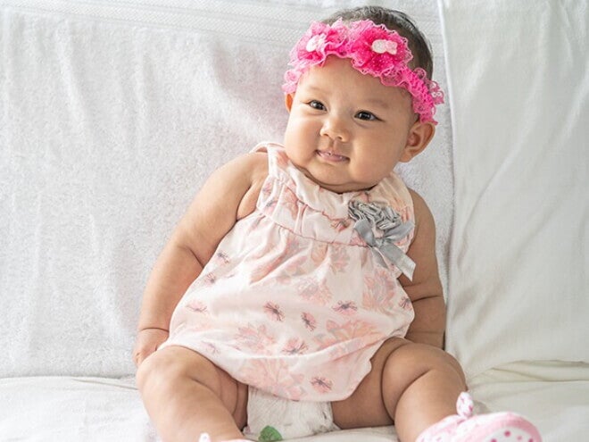 Bebê recém nascida usando vestido florido e laço bordado na cabeça. Bebê recém nascida usando vestido florido e laço bordado na cabeça.