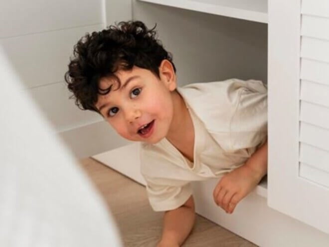 Menino faceiro brincando de se esconder na cômoda Menino faceiro brincando de se esconder na cômoda