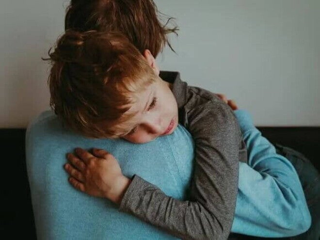 Luto infantil Um menino com olhar triste recebe o abraço de seu pai.