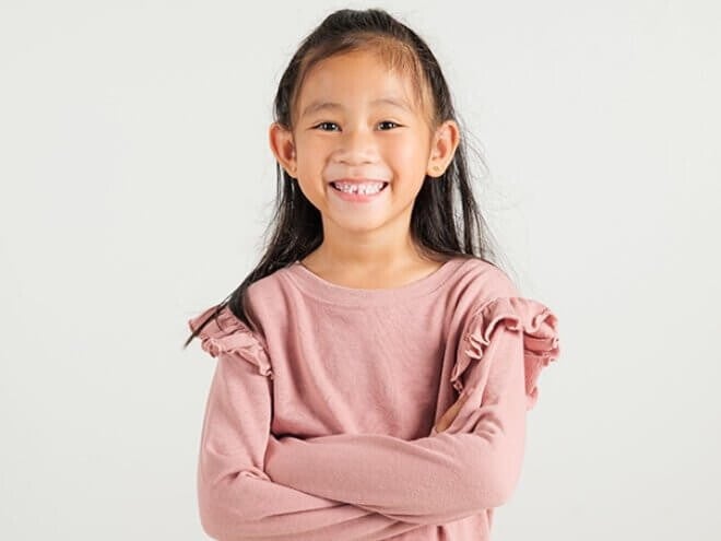 Menina asiática sorrindo com os braços cruzados em frente a uma parede clara Menina asiática sorrindo com os braços cruzados em frente a uma parede clara