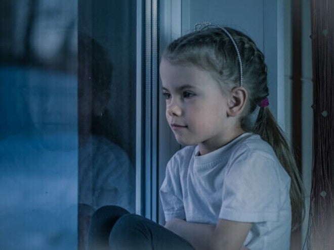 Menina de camiseta branca sentada no parapeito da janela, olhando para fora em um dia escuro.