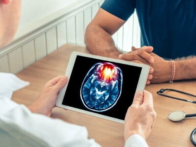 Um médico de jaleco branco mostra um tablet com uma imagem de ressonância magnética de um cérebro para um paciente. A imagem ilustra as graves consequências de doenças como a meningite B.