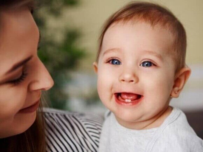 Nascimento dos dentes bebê Bebê sorrindo no colo da mãe, com os primeiros dentinhos visíveis, ilustrando o processo do nascimento dos dentes do bebê.