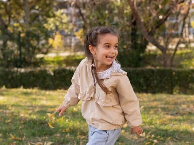 Uma menina de aproximadamente 4 anos brincando ao ar livre em um parque, com um casaco bege e tranças. Uma menina de aproximadamente 4 anos brincando ao ar livre em um parque, com um casaco bege e tranças.