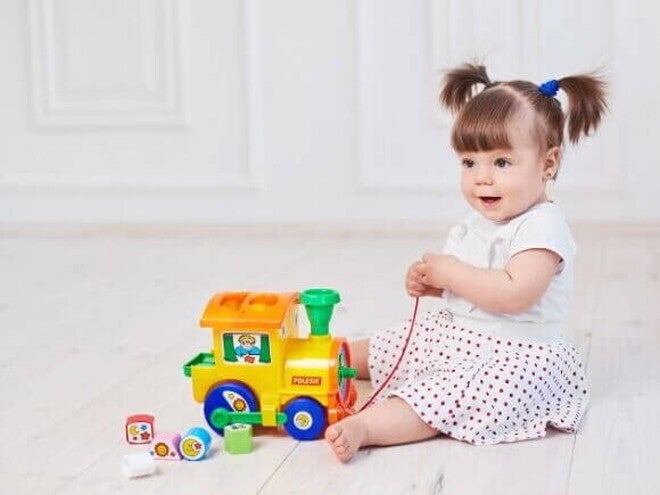 Bebê sentada no chão segurando um trenzinho de brinquedo Bebê sentada no chão segurando um trenzinho de brinquedo