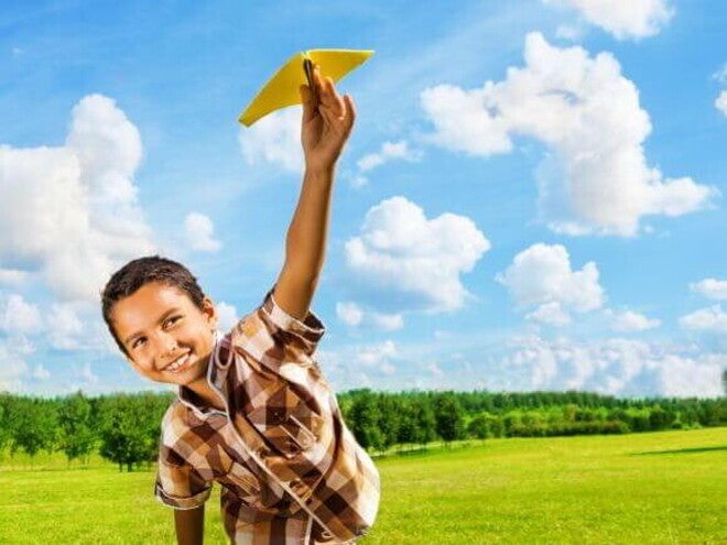 Menino sorridente com aproximadamente 07 anos brincando em um campo verde com um aviãozinho de brinquedo. Menino sorridente com aproximadamente 07 anos brincando em um campo verde com um aviãozinho de brinquedo.