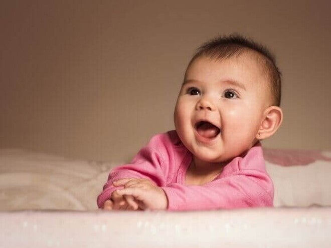 Bebê sorridente deitada de bruços na cama usando uma roupa cor de rosa. Bebê sorridente deitada de bruços na cama usando uma roupa cor de rosa.