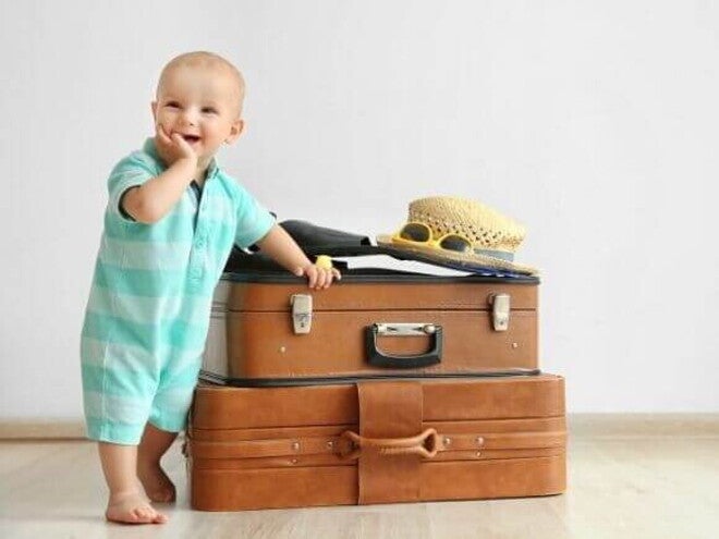Bebê sorrindo, com a mão na boca, apoiado em malas de viagem. Bebê sorrindo, com a mão na boca, apoiado em malas de viagem.