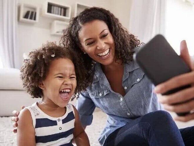 Sentadas no chão, mãe e filha sorriem ao tirar uma foto com o celular. As duas apresentam uma personalidade parecida. Sentadas no chão, mãe e filha sorriem ao tirar uma foto com o celular. As duas apresentam uma personalidade parecida.