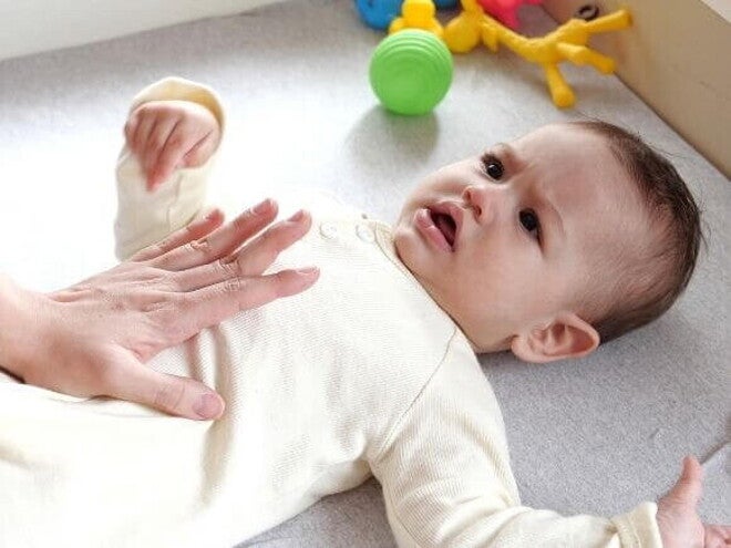 Mão de um adulto massageando suavemente a barriga de um bebê deitado, que parece estar com cólica ou outro desconforto.