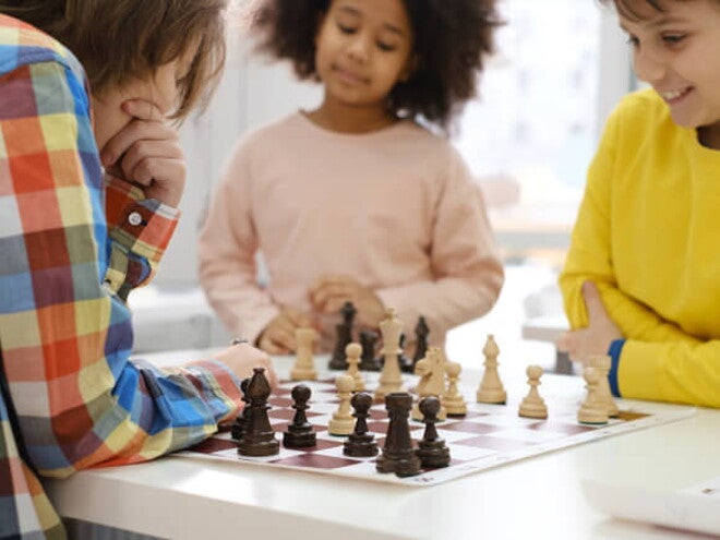 três crianças ao redor de mesa jogando xadrez três crianças ao redor de mesa jogando xadrez