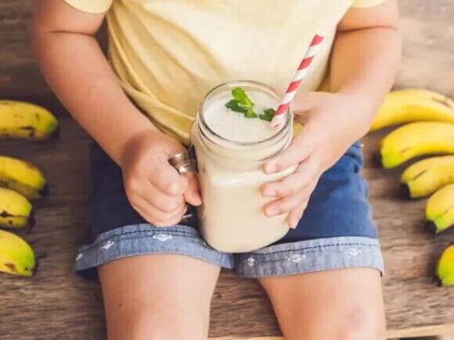 3 receitas de vitaminas de frutas e seus benefícios para as crianças criança sentada ao redor de algumas bananas, segurando vitamina