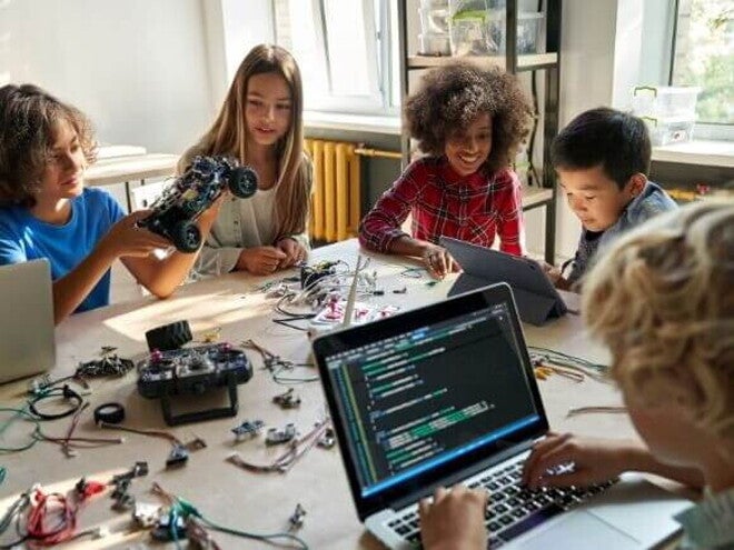 Grupo de crianças sentadas em uma mesa com várias ferramentas tecnológicas. Grupo de crianças sentadas em uma mesa com várias ferramentas tecnológicas.