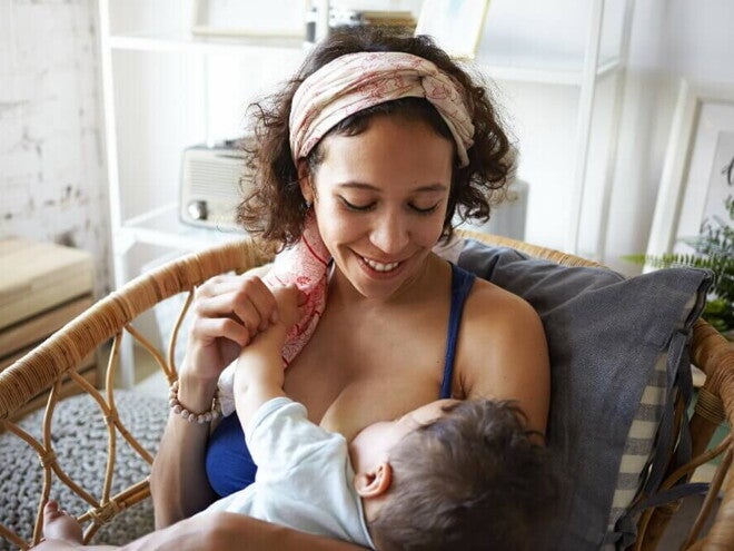 Mãe sentada e sorrindo, amamentando um bebê em seu colo Mãe sentada e sorrindo, amamentando um bebê em seu colo